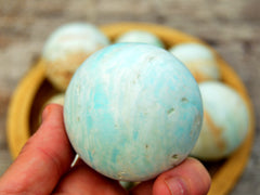 One blue caribbean calcite sphere crystal 55mm on hand with background with some crystaks inside a bowl on wood table