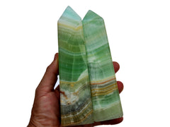 Two large green pistachio calcite crystal obelisks 145mm on hand with white background