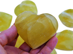 One lemon calcite heart shaped crystals 60mm on hand with background with some stones on white
