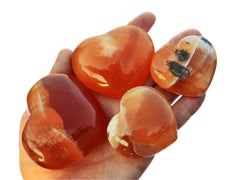 Four honey calcite crystal hearts 40mm-75mm on hand with white background