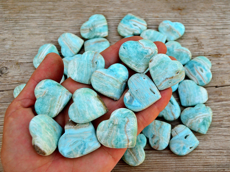 Ten blue aragonite hearts 30mm-35mm on hand with background with some hearts  on wood table