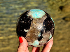 One green amazonite crystal sphere 90mm on hand with background with river landscape
