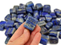 One lapis lazuli tumbled crystal 20mm on hand with background with several stones