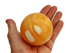 One large orange calcite  ball 80mm on hand with white background
