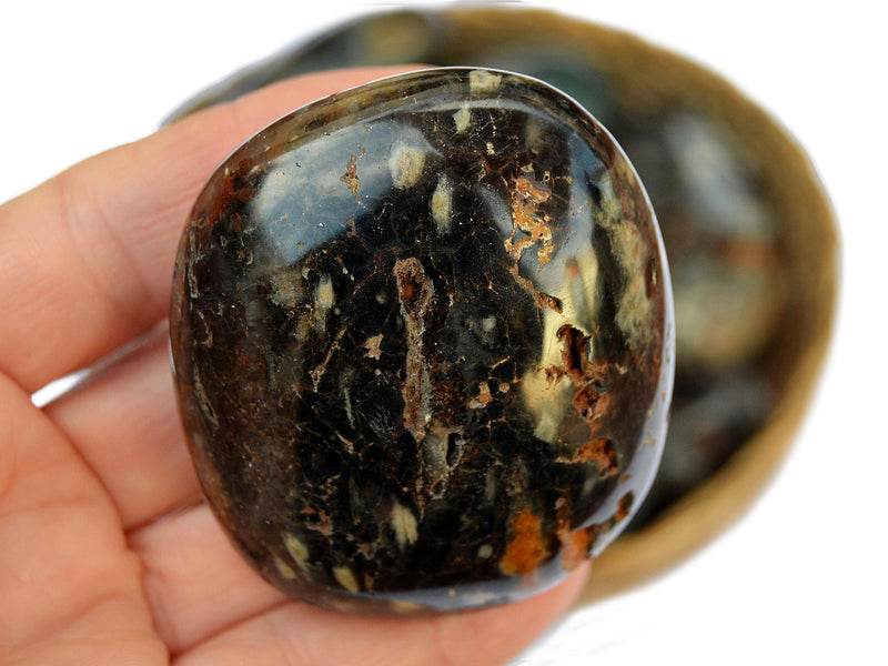 Large sea jasper palm stone 55mm on hand with background with some stones inside a basket