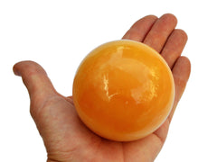 One large orange calcite crystal ball 75mm on hand with white background