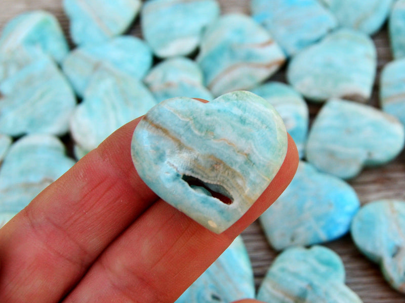 One small blue aragonite druzy heart 30mm on hand with background with severals hearts on wood table
