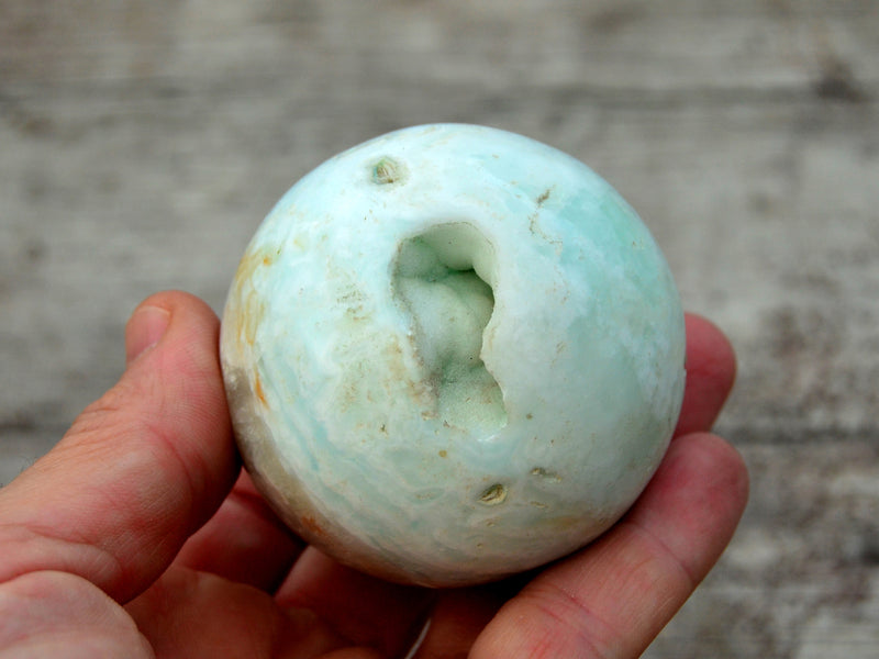 One caribbean calcite druzy sphere crystal 50mm on hand with wood background