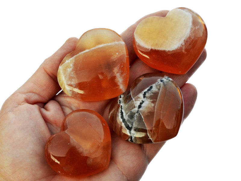 Four honey calcite crystal hearts 40mm-50mm on hand with white background