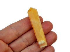 One small orange calcite tower mineral on hand with white background