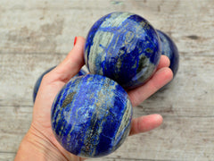 Two blue lapis lazuli sphere crystals 75mm on hand with wood background