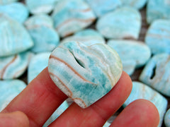 One blue aragonite druzy heart 30mm on hand with background with severals hearts on wood table