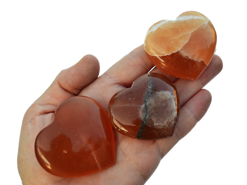 Three honey calcite crystal hearts 40mm-50mm on hand with white background