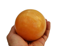 One large orange calcite ball 80mm on hand with white background