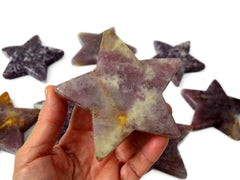 One purple lepidolite star mineral on hand with background with some stars on white