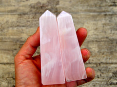 Two pink mangano calcite obelisks 90mm on hand with wood background