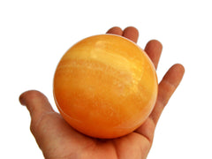 One orange calcite sphere crystal 80mm on hand with white background