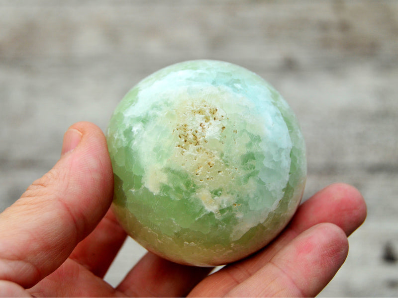 One caribbean calcite crystal ball 50mm on hand with wood background