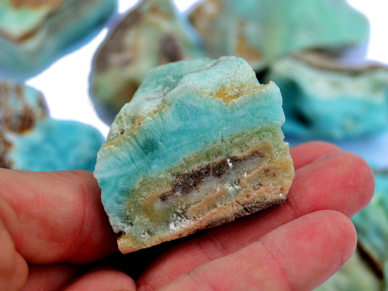One small blue aragonite rough stone on hand with background with some crystals on white