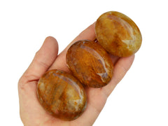 Three yellow hematoid quartz palm stones 50mm-55mm on hand with white background