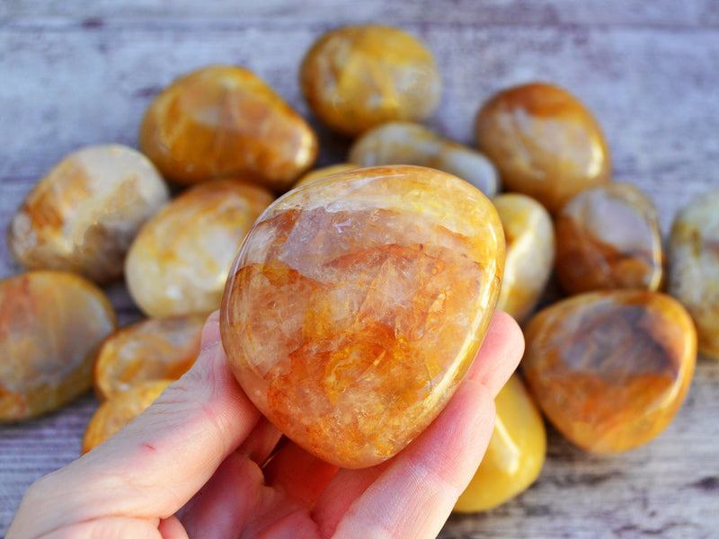 One big golden healer tumbled mineral on hand with background with some stones on wood table