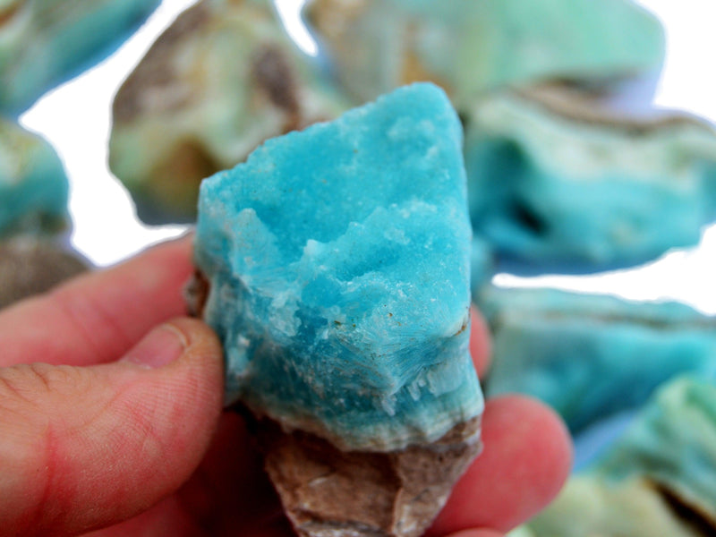 One small blue aragonite raw stone on hand with background with some crystals on white