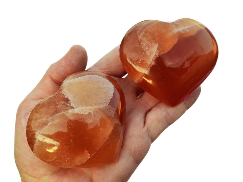 Three honey calcite heart shaped stones 55mm-65mm on hand with white background
