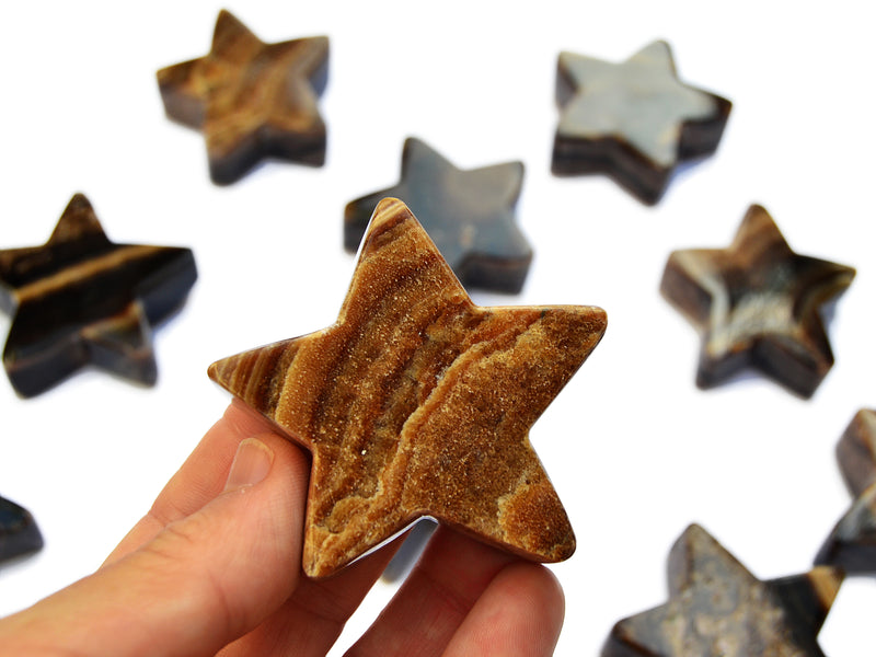 One chocolate calcite star carved mineral 55mm on hand with background with some stars on white