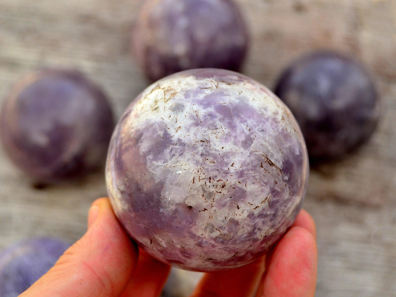 One purple lepidolite crystal sphere 50mm on hand with background with some balls on wood table