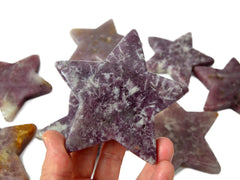 One purple lepidolite star carved crystal on hand with background with some stars on white