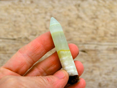 One pistachio calcite faceted point 65mm on hand with wood background