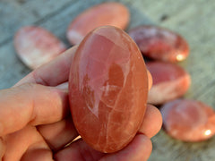 One rose calcite palm stone 50mm on hand with background with some stones on wood table