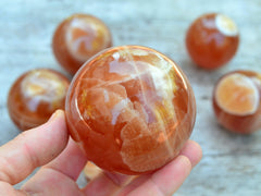 One honey calcite crystal ball 70mm on hand with background with some minerals on wood table