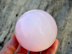 One large pink mangano calcite crystal ball 65mm on hand with wood background