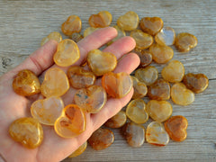 Ten yellow hematoid quartz hearts 30mm on hand with some stones on wood table
