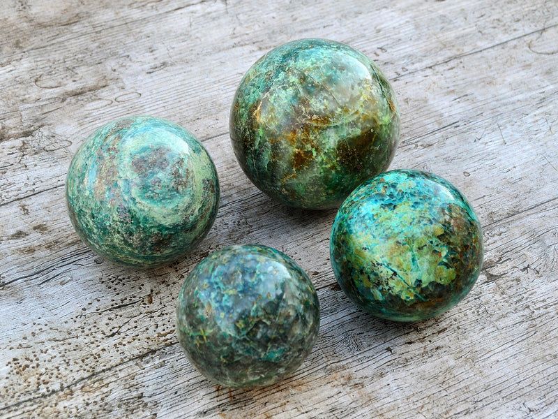 Four green chrysocolla sphere crystals 65mm-100mm on wood background