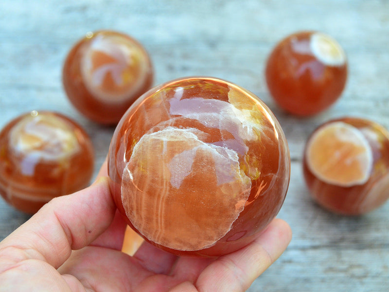 One honey calcite crystal sphere 70mm on hand with background with some minerals on wood table