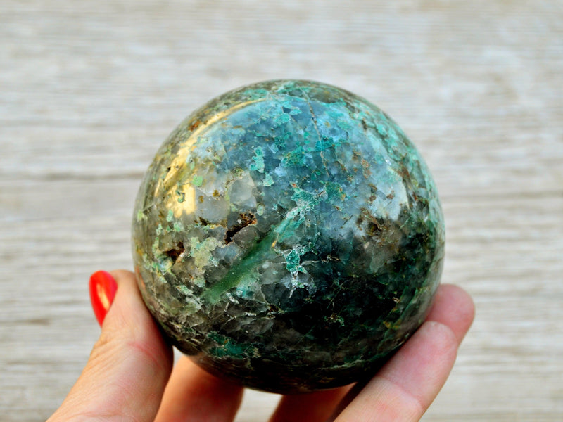 Big chrysocolla sphere 75mm on hand with river landscape background