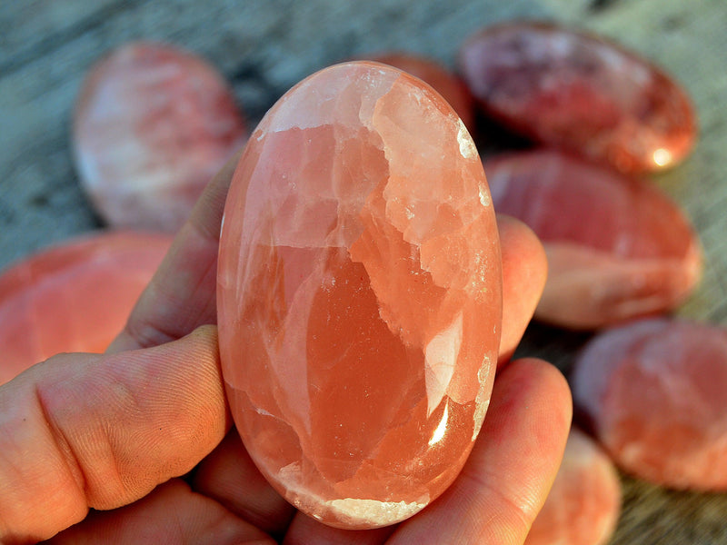 One rose calcite palm stone 65mm on hand with background with some stones on wood table
