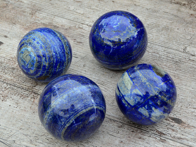 Four blue lapis lazuli sphere crystals 65mm-90mm on wood table