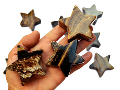 Three chocolate calcite star carved crystals 55mm-60mm on hand with background with some stars on white