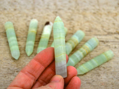 One pistachio calcite faceted point 65mm on hand with background with some points