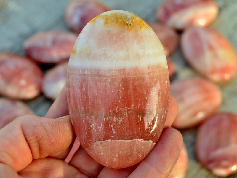 One rose calcite palm stone 60mm on hand with background with some stones on wood table