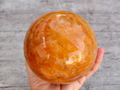 Large golden healer quartz sphere 100mm on hand with wood background