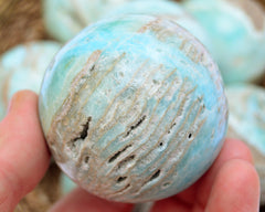 Druzy blue aragonite sphere stone 70mm on hand with background with some crystals