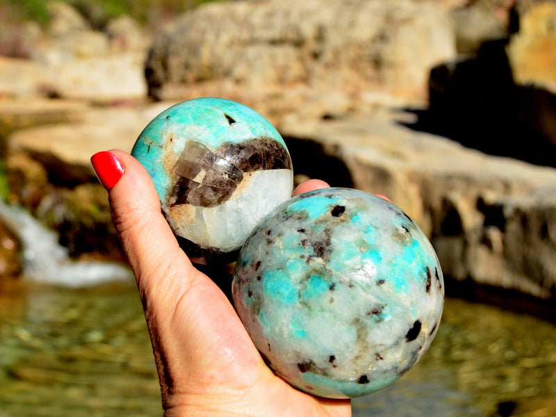 Two green amazonitecrystal balls 60mm-70mm on hand with river landscape background