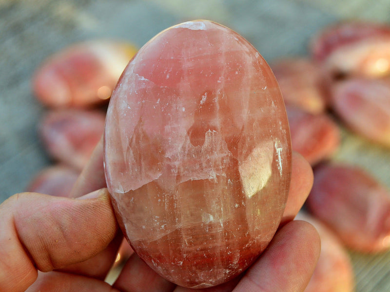 One rose calcite palm stone 50mm on hand with background with some crystals on wood table