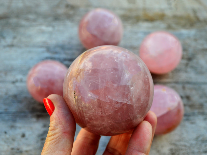 One  rose quartz sphere crystal 70mm on hand with background with some balls on wood table