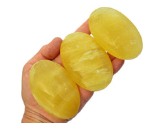 Three large lemon calcite palm crystals 75mm on hand with white background