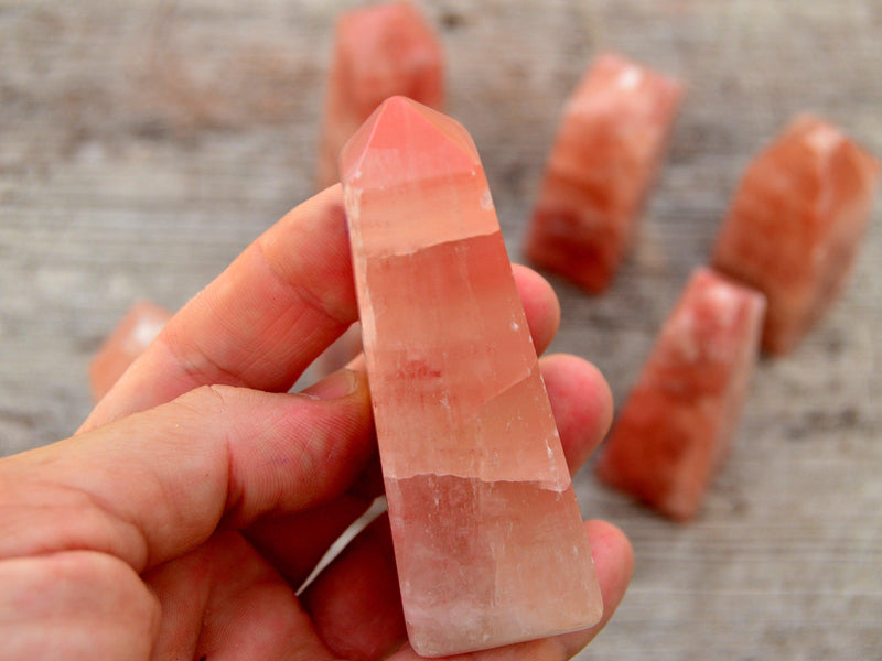 One rose calcite towers 85mm on hand with background with some crystals on wood table